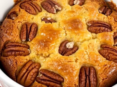 A warm, golden sweet potato pecan dump cake served in a white bowl, showing a bubbly, textured top.