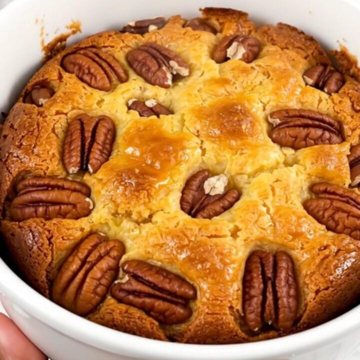 A warm, golden sweet potato pecan dump cake served in a white bowl, showing a bubbly, textured top.