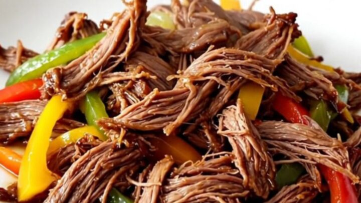 A close-up of tender, shredded fajita beef with colorful bell peppers served on a plate.
