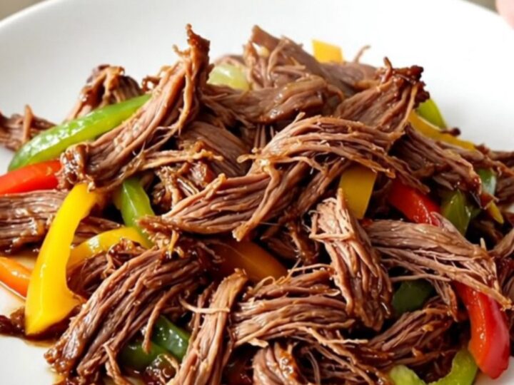 A close-up of tender, shredded fajita beef with colorful bell peppers served on a plate.