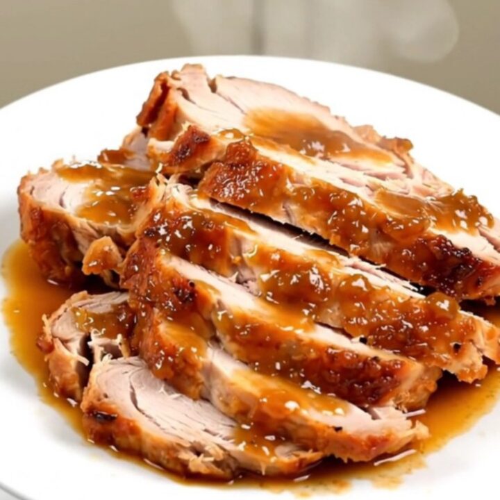 A succulent, sliced turkey breast with a glossy apple glaze on a white plate.