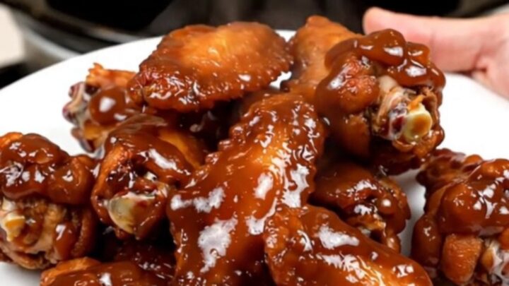 A top-down view of raw chicken wings and onions being prepared in a black slow cooker on a white countertop.