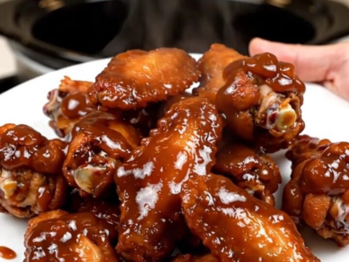 A top-down view of raw chicken wings and onions being prepared in a black slow cooker on a white countertop.