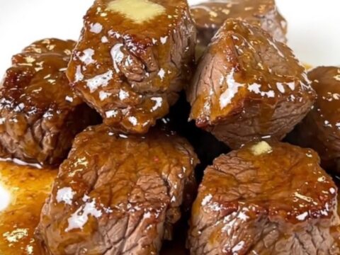 A plate of tender, glossy slow cooker steak bites with diced jalapenos in a rich butter glaze.
