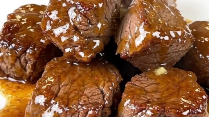 A plate of tender, glossy slow cooker steak bites with diced jalapenos in a rich butter glaze.