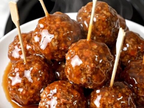 A plate of glossy, peach-glazed beef meatballs on wooden skewers ready to serve.