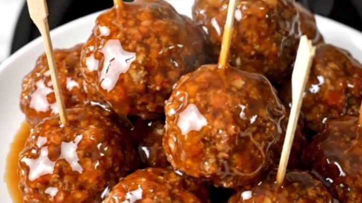 A plate of glossy, peach-glazed beef meatballs on wooden skewers ready to serve.