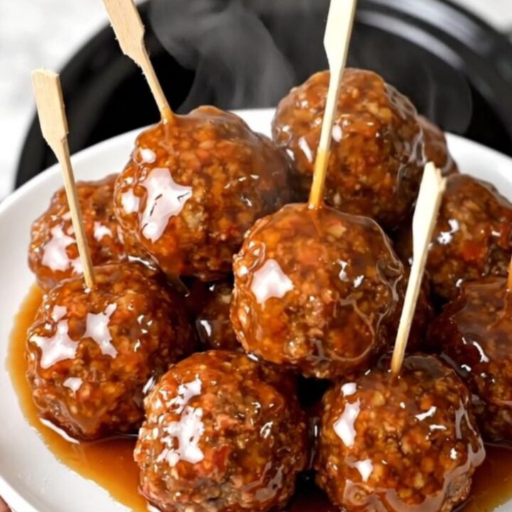 A plate of glossy, peach-glazed beef meatballs on wooden skewers ready to serve.