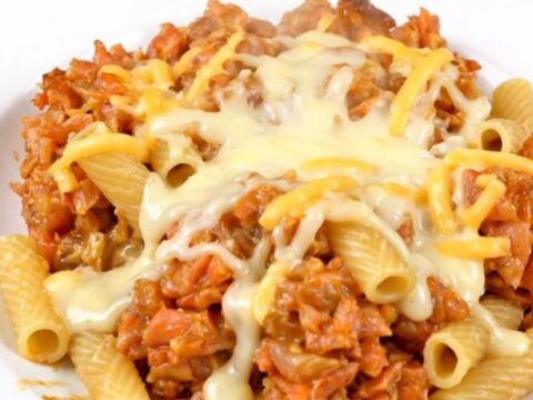 A top-down view of a black slow cooker filled with ziti, sliced mushrooms, and garlic seasoning before cooking.
