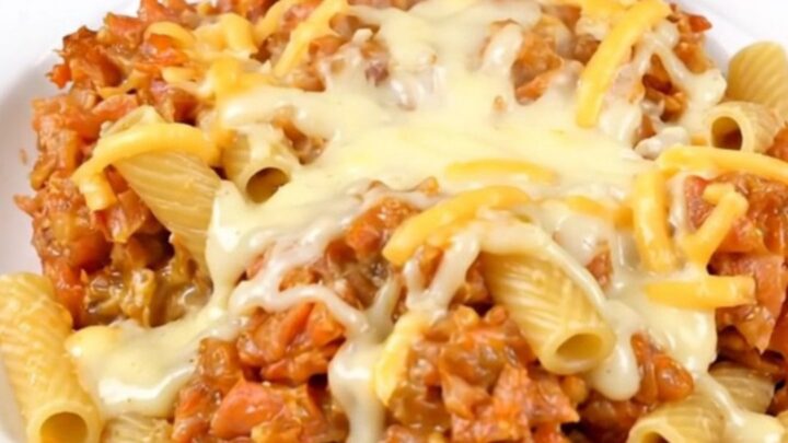 A top-down view of a black slow cooker filled with ziti, sliced mushrooms, and garlic seasoning before cooking.