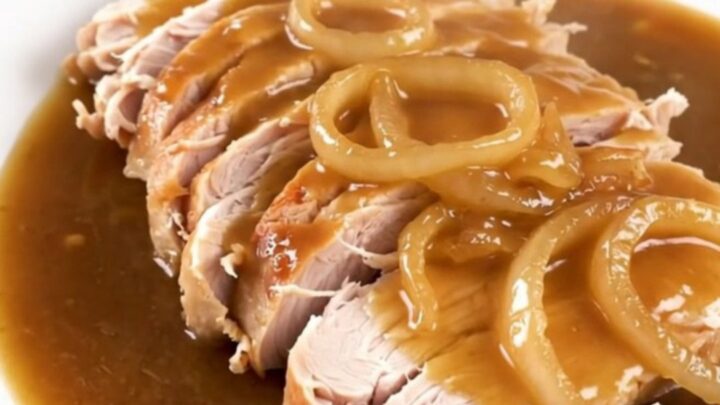 Slow cooker turkey breast topped with caramelized onions and rich gravy in a ceramic pot.