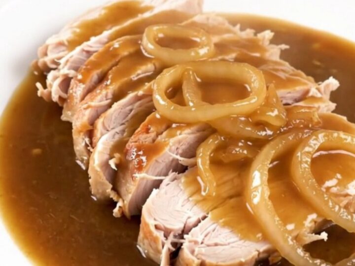 Slow cooker turkey breast topped with caramelized onions and rich gravy in a ceramic pot.