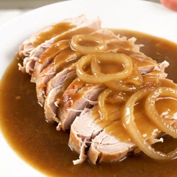 Slow cooker turkey breast topped with caramelized onions and rich gravy in a ceramic pot.