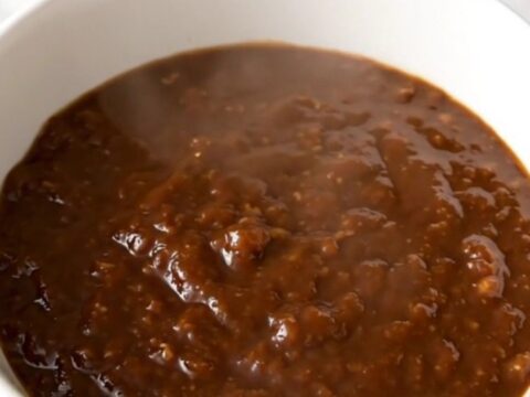 A steaming bowl of thick molasses barbecue beef chili in a white bowl on a kitchen counter.