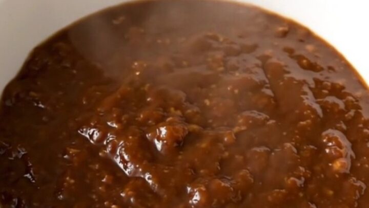 A steaming bowl of thick molasses barbecue beef chili in a white bowl on a kitchen counter.