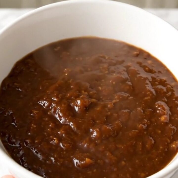 A steaming bowl of thick molasses barbecue beef chili in a white bowl on a kitchen counter.
