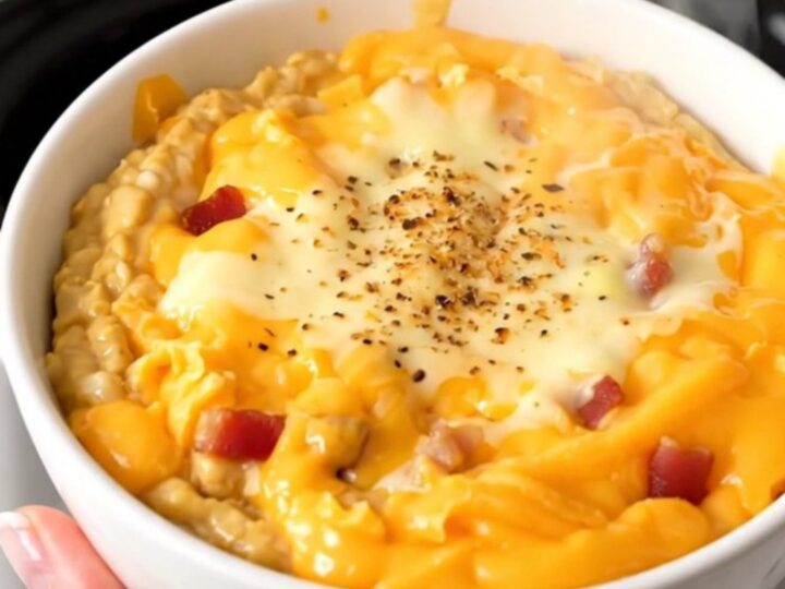 A white ceramic bowl filled with warm, melted bacon cheddar ranch dip, garnished with crispy bacon bits.