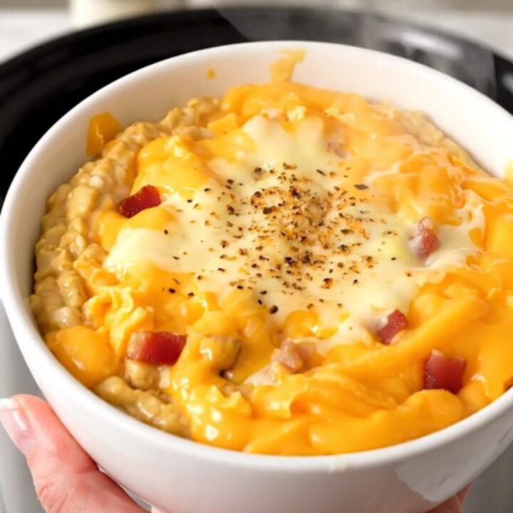 A white ceramic bowl filled with warm, melted bacon cheddar ranch dip, garnished with crispy bacon bits.
