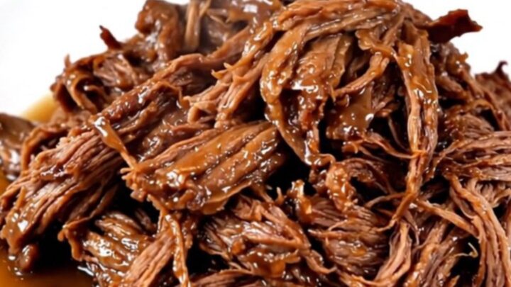 A close-up of a slow cooker filled with a raw chuck roast, sliced onions, and bell peppers.