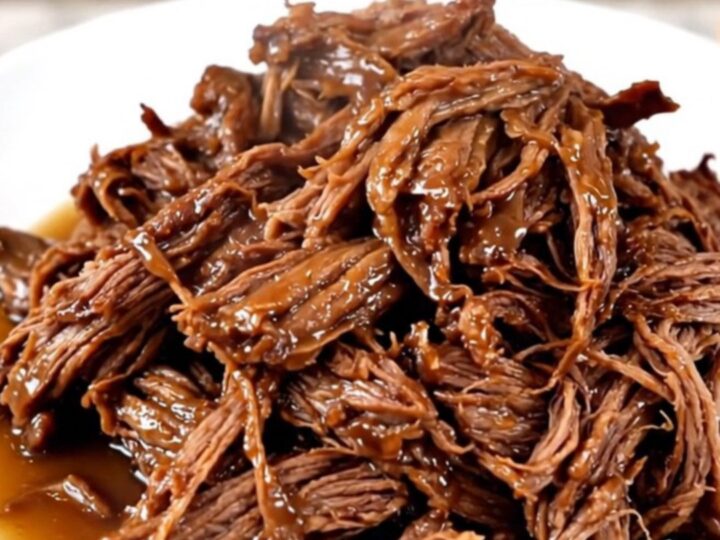 A close-up of a slow cooker filled with a raw chuck roast, sliced onions, and bell peppers.