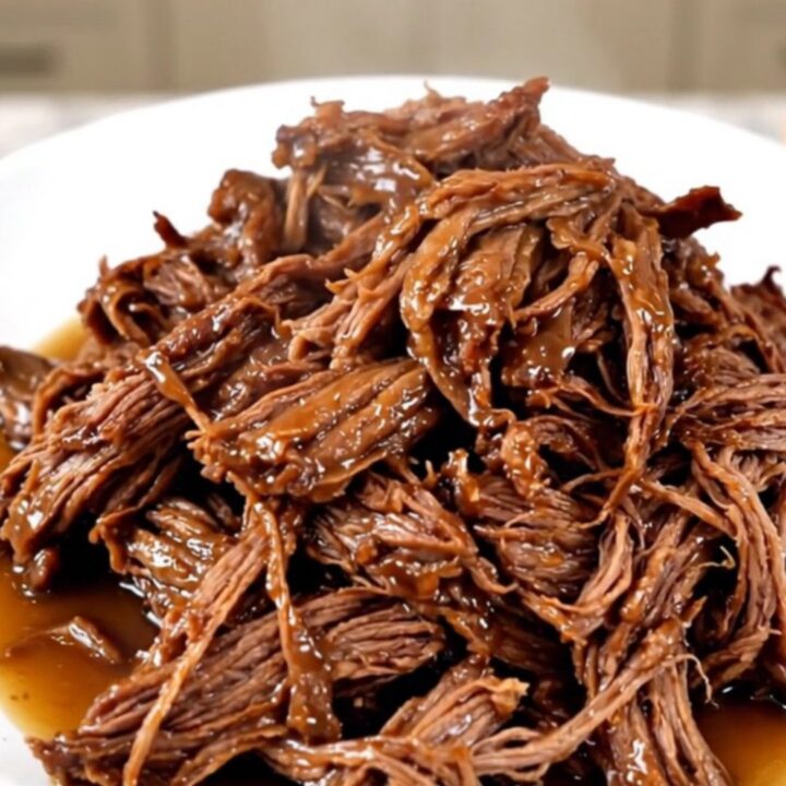 A close-up of a slow cooker filled with a raw chuck roast, sliced onions, and bell peppers.