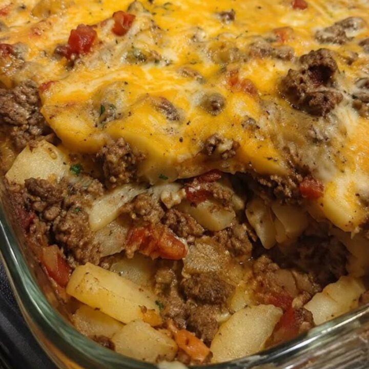 A hearty serving of cheesy hamburger potato casserole being lifted from a glass baking dish with a spatula.