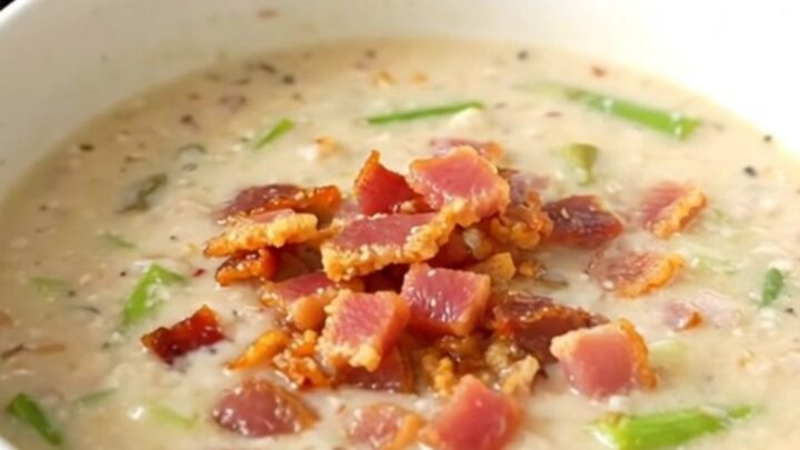 A steaming bowl of creamy bacon and asparagus chowder on a white background.