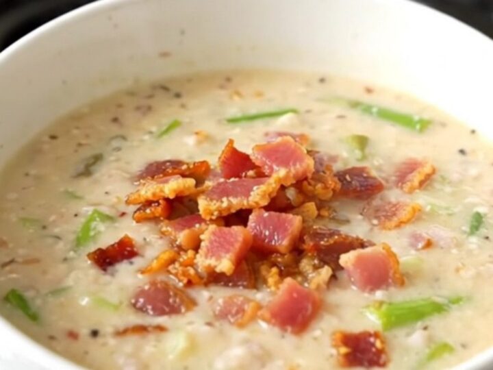 A steaming bowl of creamy bacon and asparagus chowder on a white background.