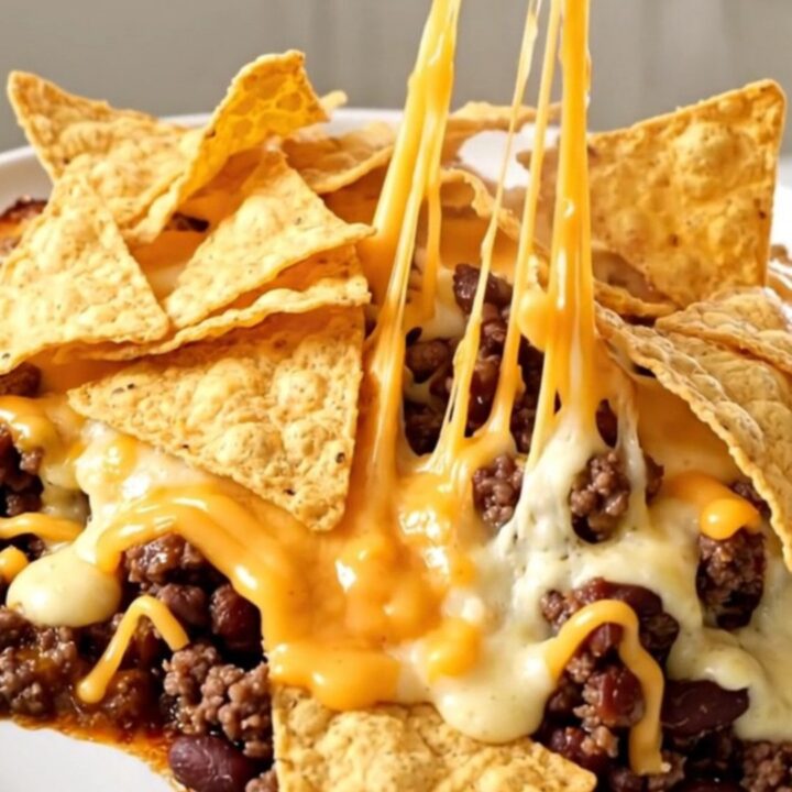 A top-down view of a slow cooker filled with a rich, cheesy beef and bean casserole topped with tortilla chips.