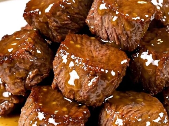 A white plate filled with glossy, glazed honey mustard steak bites with a soft-focus background.