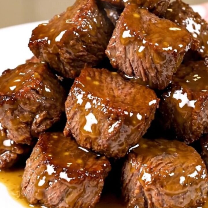 A white plate filled with glossy, glazed honey mustard steak bites with a soft-focus background.