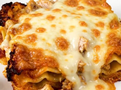 A close-up of a serving of creamy chicken bacon ranch lasagna on a white plate.