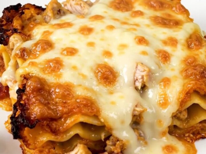 A close-up of a serving of creamy chicken bacon ranch lasagna on a white plate.