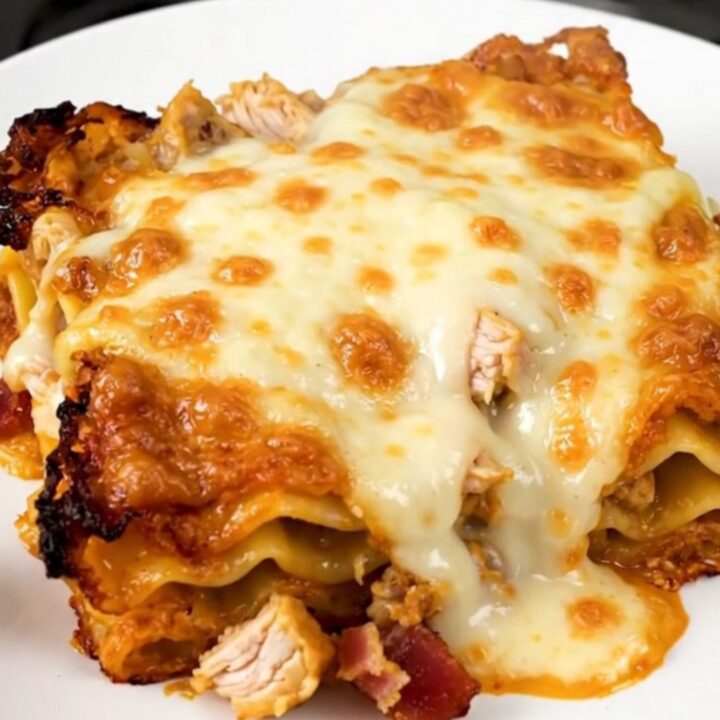 A close-up of a serving of creamy chicken bacon ranch lasagna on a white plate.