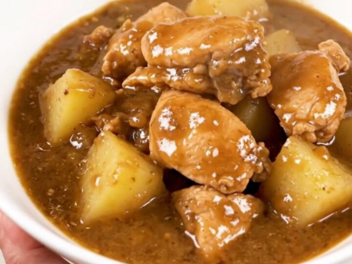 A steaming, glossy chicken and potato stew served in a wide white bowl on a kitchen counter.
