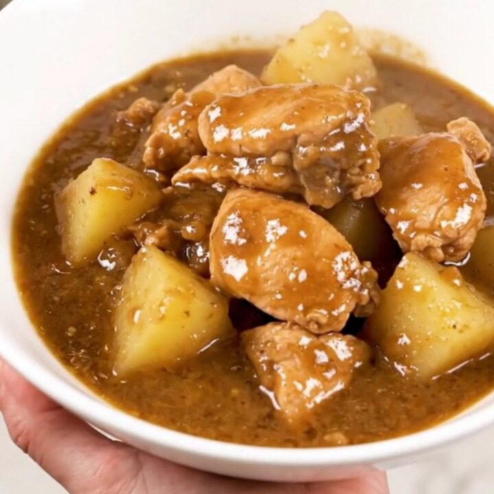 A steaming, glossy chicken and potato stew served in a wide white bowl on a kitchen counter.