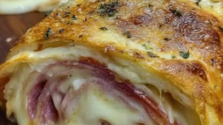 A warm, golden-brown stromboli roll resting on a wooden cutting board with oozing melted mozzarella.