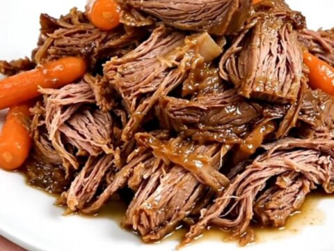 A tender beef roast and baby carrots in a slow cooker on a white quartz countertop.