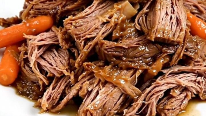 A tender beef roast and baby carrots in a slow cooker on a white quartz countertop.