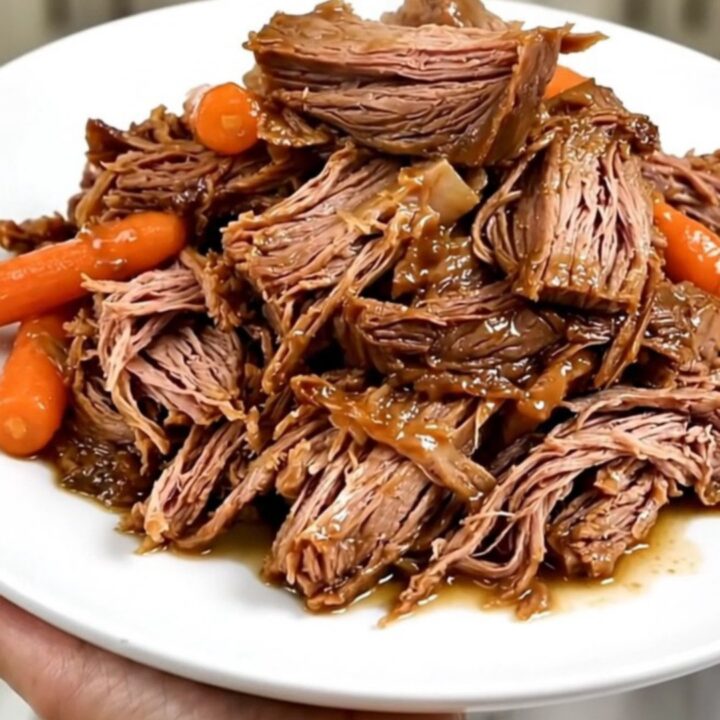 A tender beef roast and baby carrots in a slow cooker on a white quartz countertop.