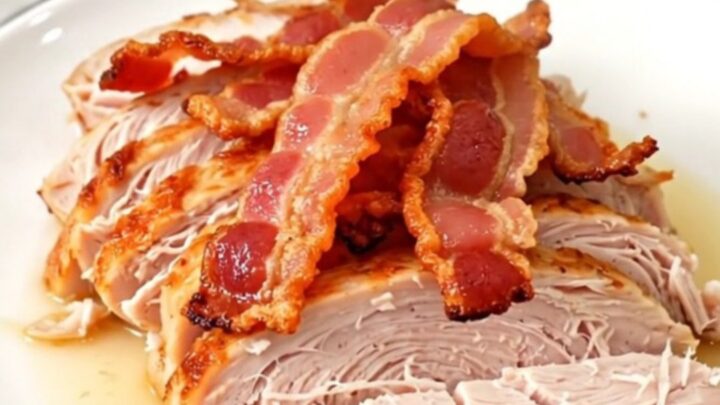 A cooked, juicy turkey breast topped with crispy bacon pieces, served on a white plate.