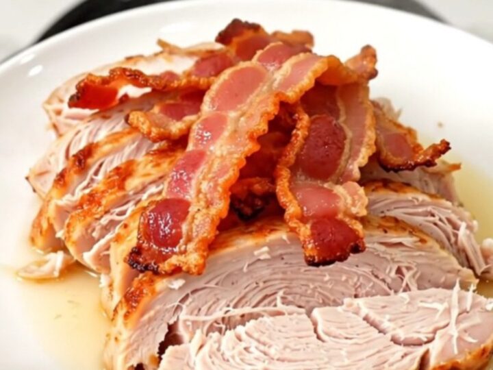 A cooked, juicy turkey breast topped with crispy bacon pieces, served on a white plate.