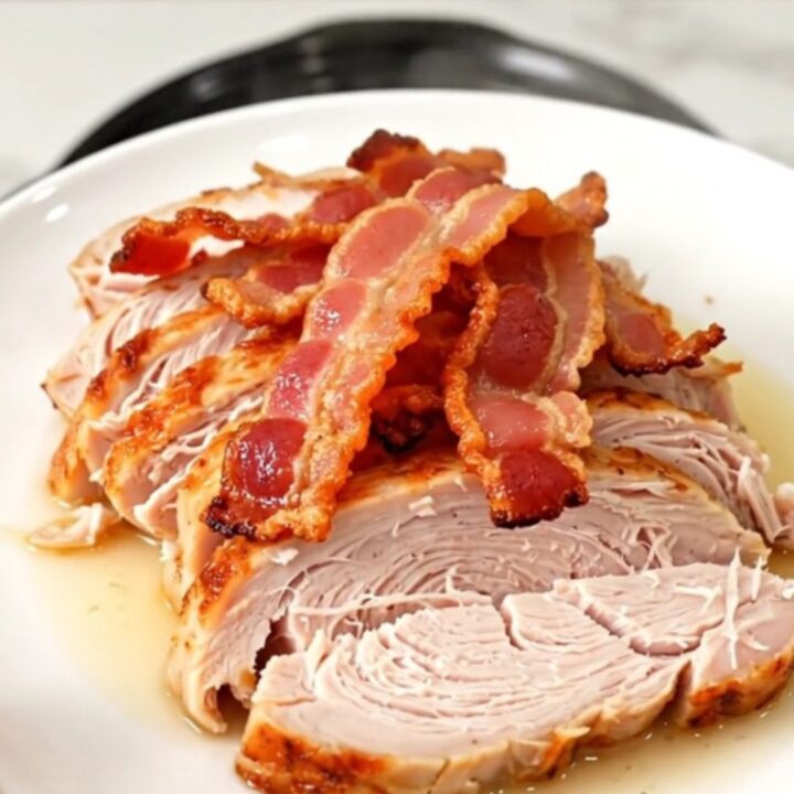 A cooked, juicy turkey breast topped with crispy bacon pieces, served on a white plate.