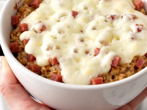 A white bowl filled with creamy, melted pastrami and Swiss cheese dip, showing a rich and glossy texture.