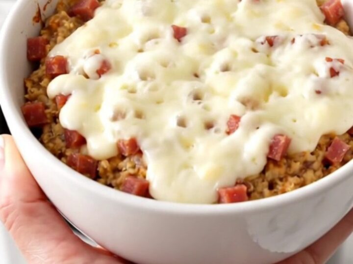 A white bowl filled with creamy, melted pastrami and Swiss cheese dip, showing a rich and glossy texture.