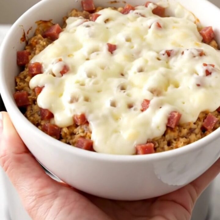 A white bowl filled with creamy, melted pastrami and Swiss cheese dip, showing a rich and glossy texture.