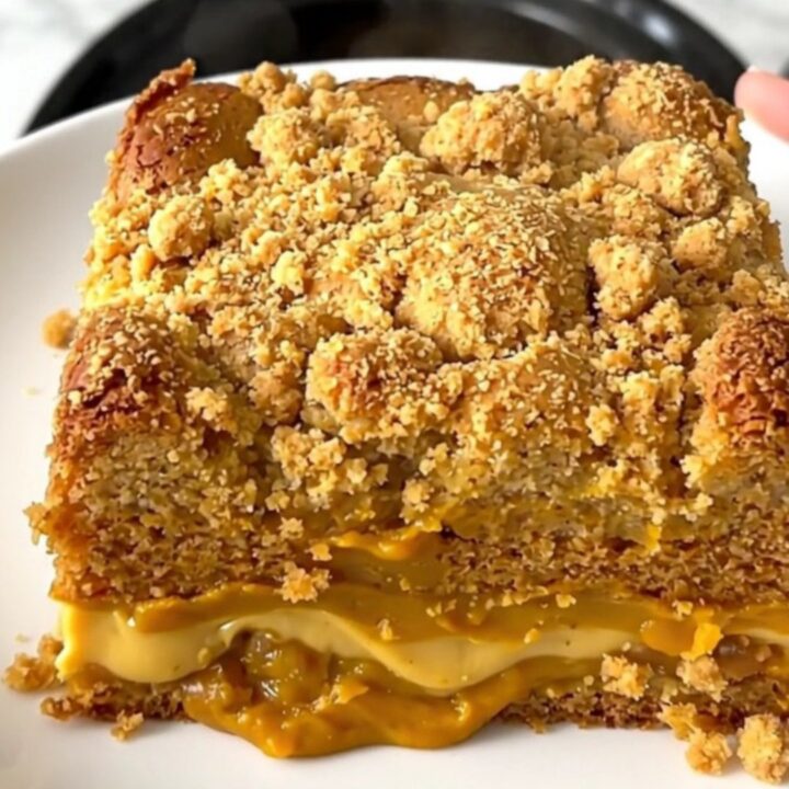 A top-down view of a black slow cooker filled with a creamy pumpkin chai mixture topped with a light layer of cake mix.
