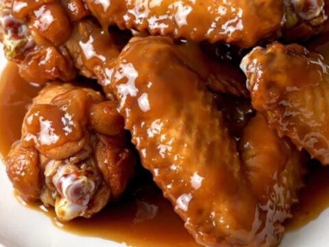 A plate of glazed, steaming chicken wings with diced apples in a slow cooker.