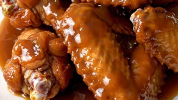 A plate of glazed, steaming chicken wings with diced apples in a slow cooker.