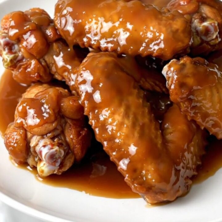 A plate of glazed, steaming chicken wings with diced apples in a slow cooker.